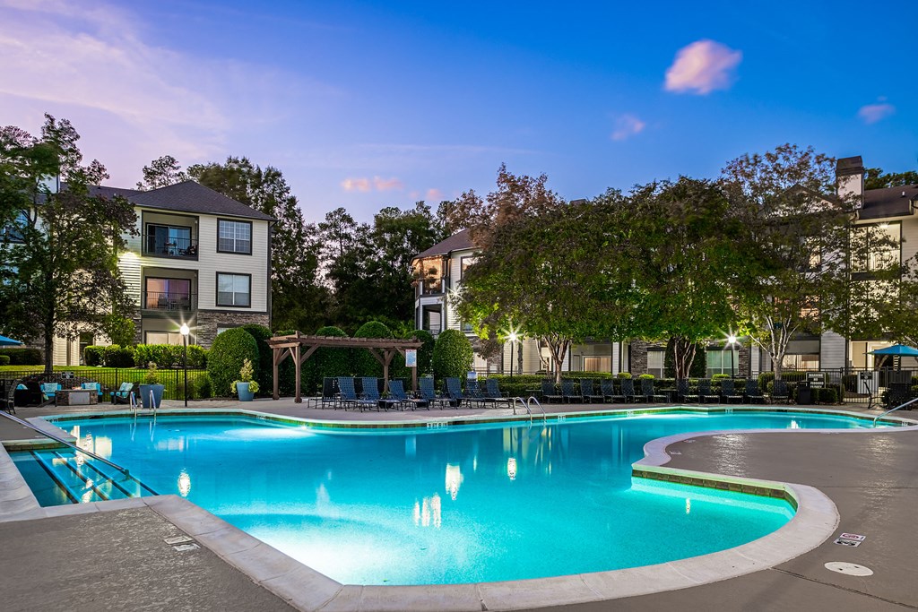 a swimming pool at night with apartments in the background