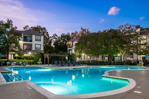 a swimming pool at night with apartments in the background