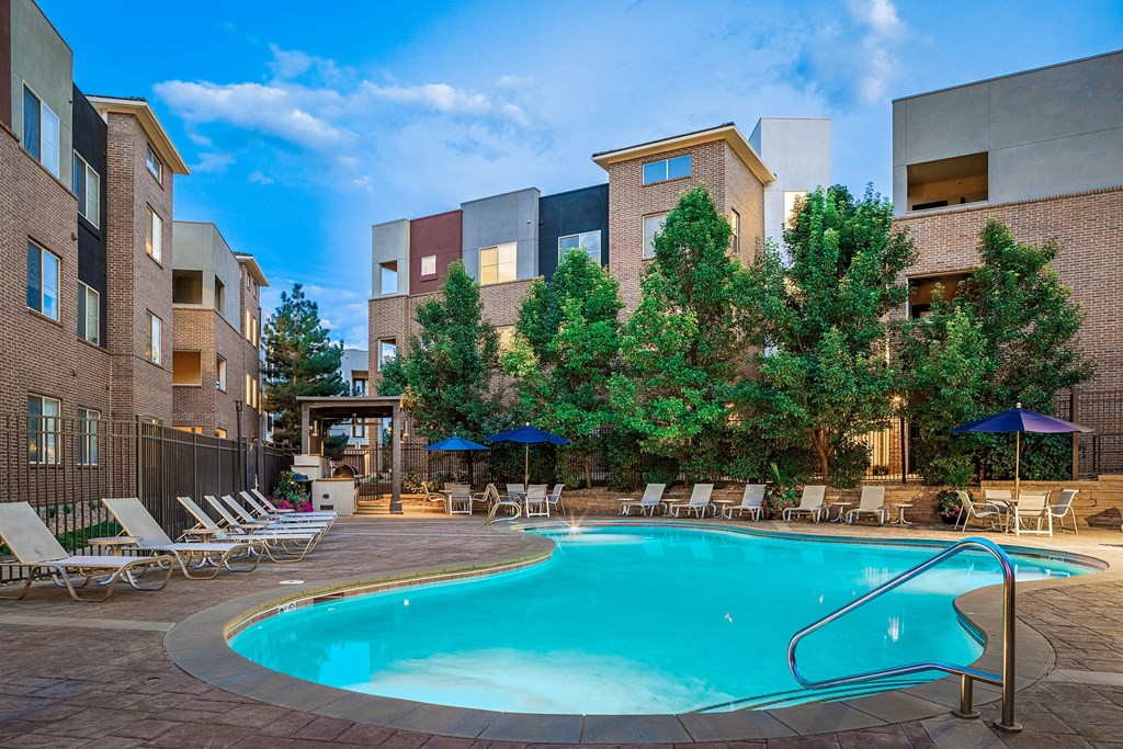 a swimming pool with chairs and umbrellas in front of an apartment building