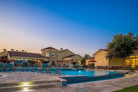 A pool surrounded by a stone patio and a house in the background.