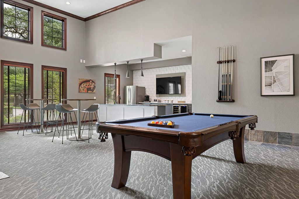 A pool table is in the middle of a room with a bar and chairs.