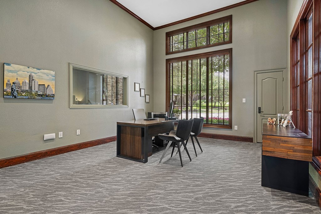 A room with a desk and chairs with a painting on the wall.