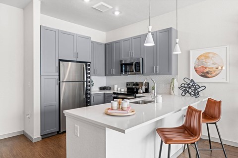 A kitchen with a white counter top and brown chairs.