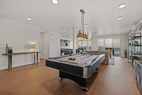 A pool table is in the middle of a room with a bar and a balcony.