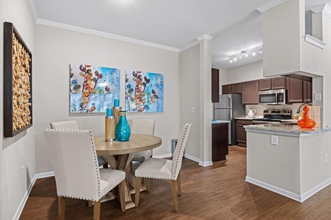 A dining room with a table and chairs and a painting on the wall.