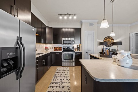 A modern kitchen with a refrigerator on the left and a clock on the wall.