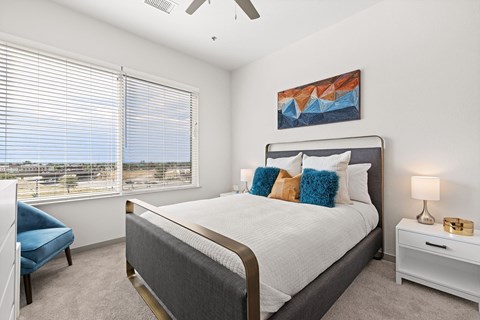 A bedroom with a large bed, a blue chair, and a ceiling fan.