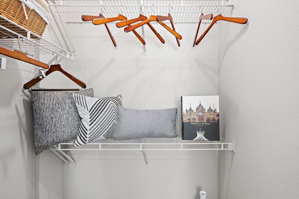 a closet with a shelf with orange hangers and pillows on it