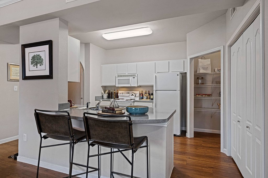 A kitchen with white cabinets and a fridge with a pantry in the background.