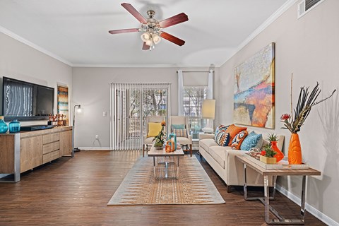 A living room with a white ceiling fan and a white couch with orange pillows.