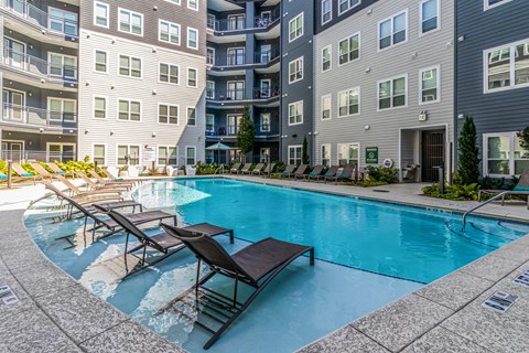 A swimming pool surrounded by lounge chairs and buildings.