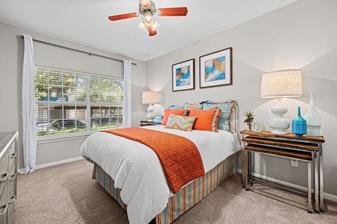 A bedroom with a bed, a table with a lamp, and a ceiling fan.