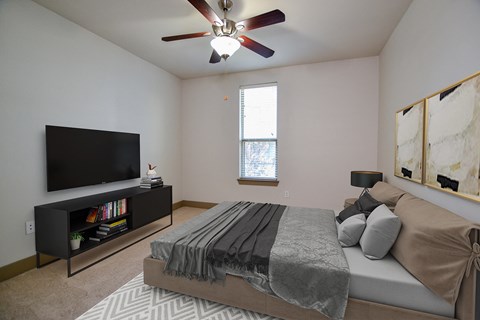 A bedroom with a bed, a television, and a ceiling fan.