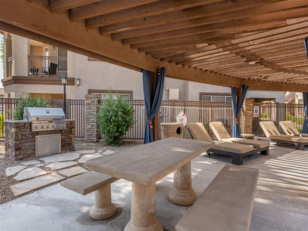 a patio with a picnic table and chairs and a grill