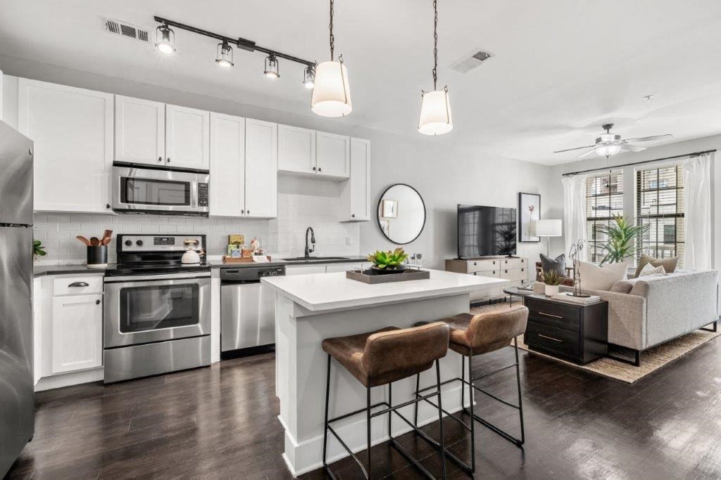 an open kitchen and living room with white cabinets and stainless steel appliances