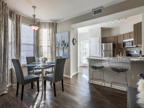 A dining room with a table set for four and chairs around it.