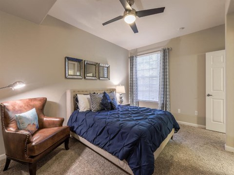 A bedroom with a bed, chair, and ceiling fan.