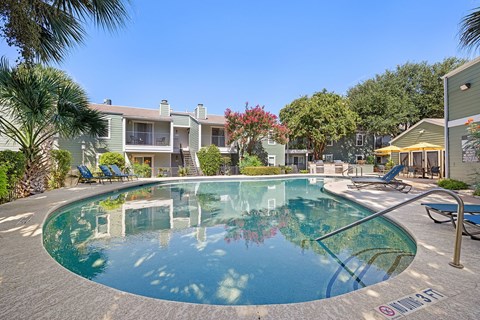 A swimming pool surrounded by palm trees and lounge chairs.