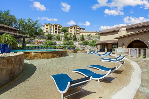 A pool area with blue lounge chairs and a stone wall.