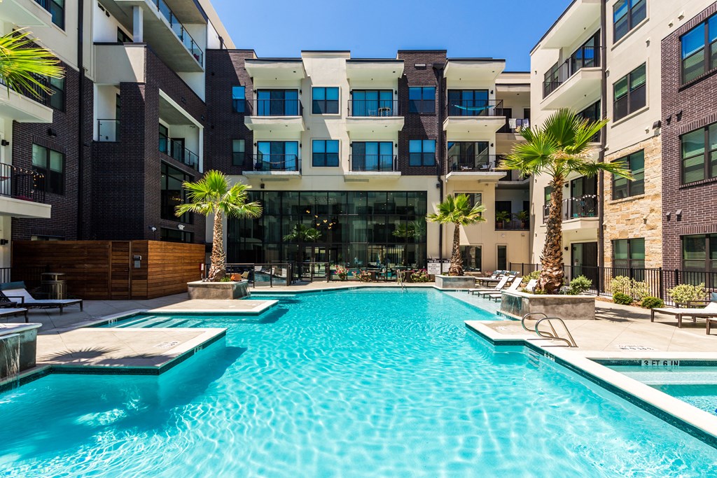 a swimming pool in front of an apartment building with palm trees
