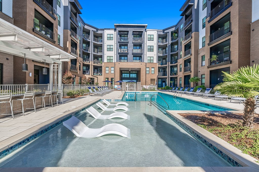 a swimming pool with white chairs in front of an apartment building