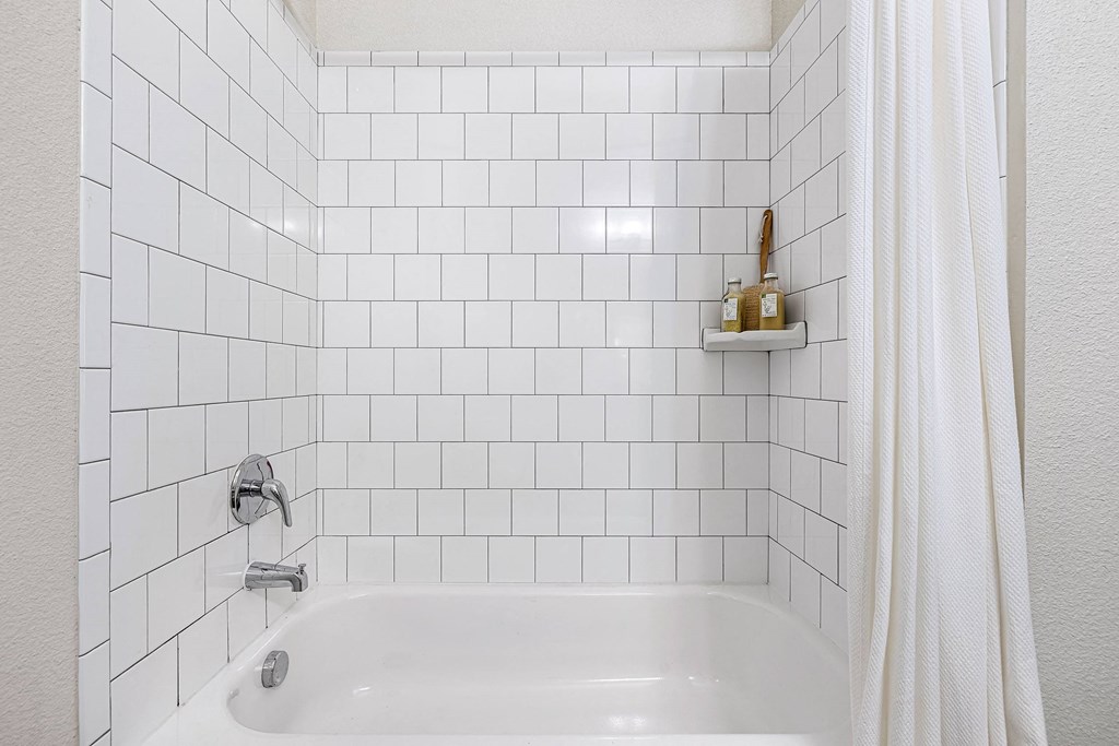 a white tiled bathroom with a bath tub and a shower curtain