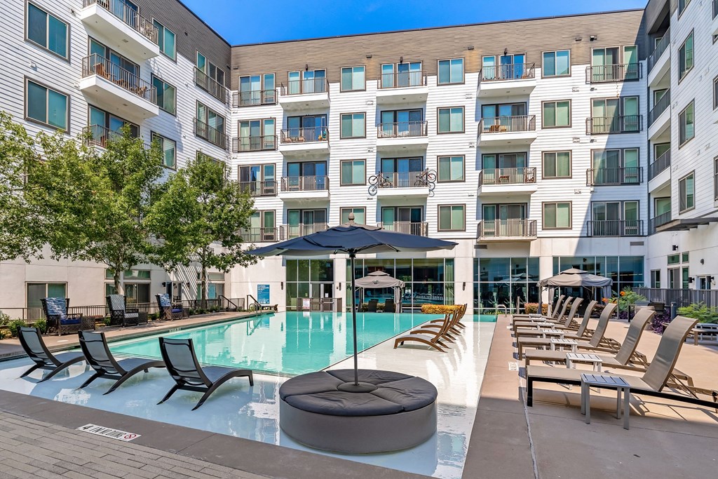 a swimming pool with chairs and umbrellas in front of an apartment building