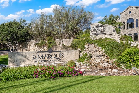 a sign for the apartments is in front of a rock wall and flowers