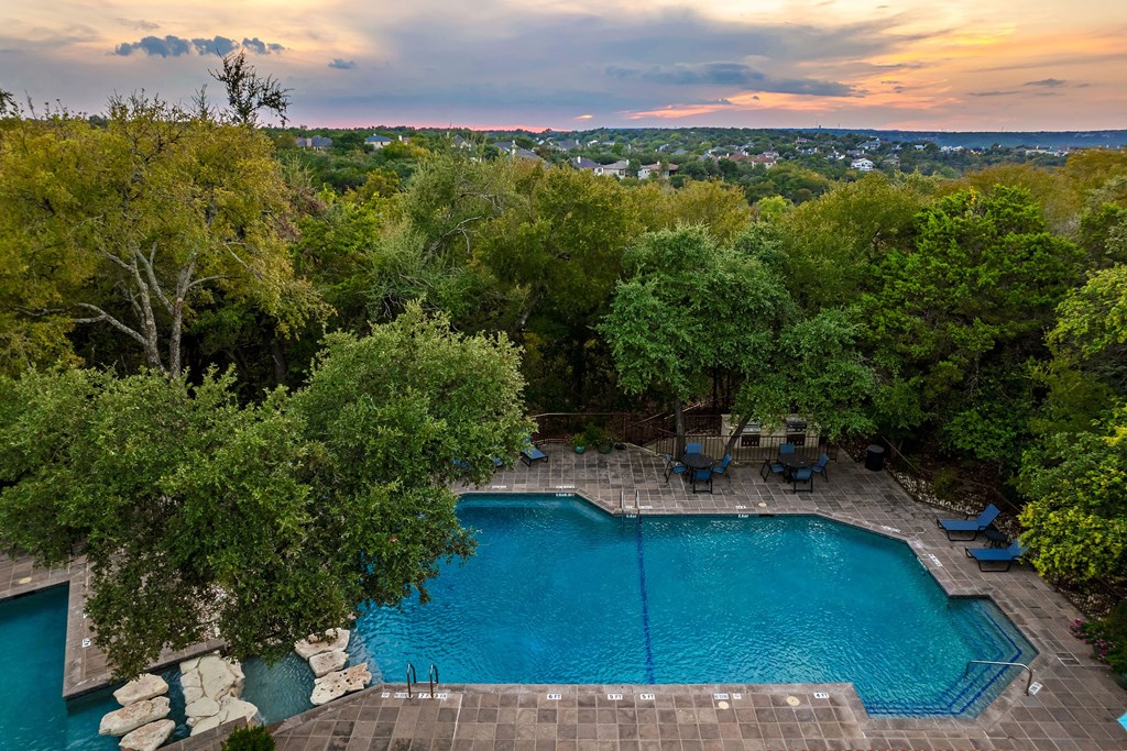 an aerial view of a pool with trees and a sunset