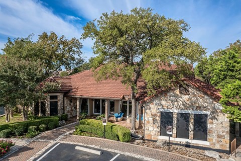 the front of a stone house with a driveway and trees