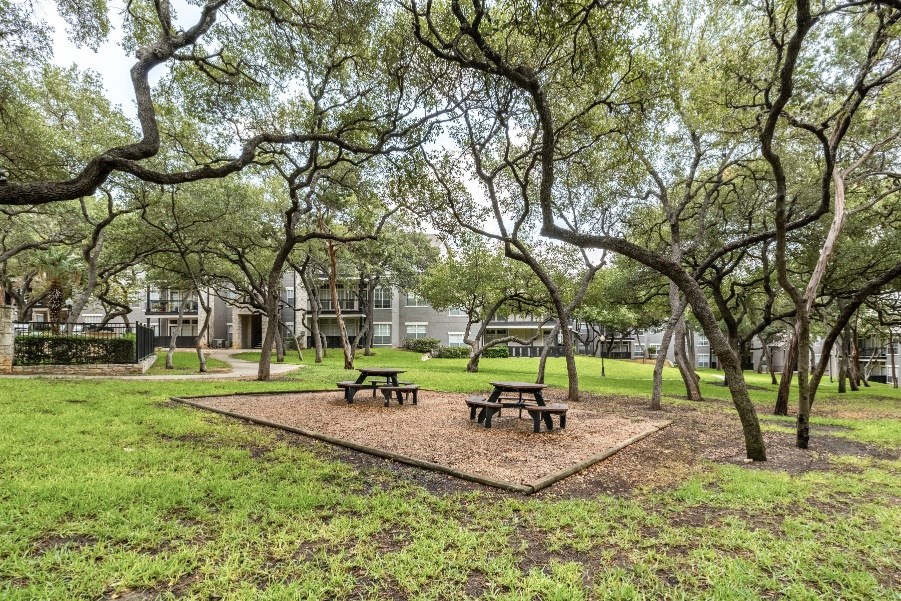 a park with picnic tables and trees with apartment buildings in the background