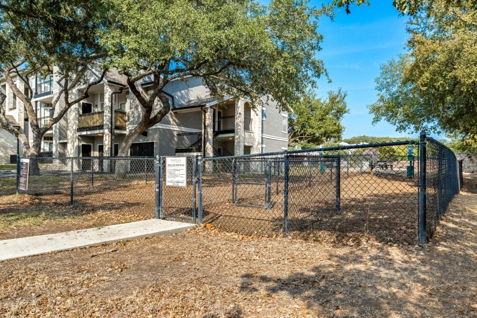 a fenced in dog park with trees and apartments in the background