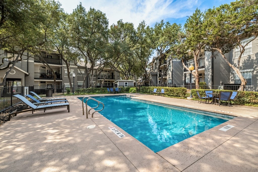 a swimming pool with chaise lounge chairs and trees in the background