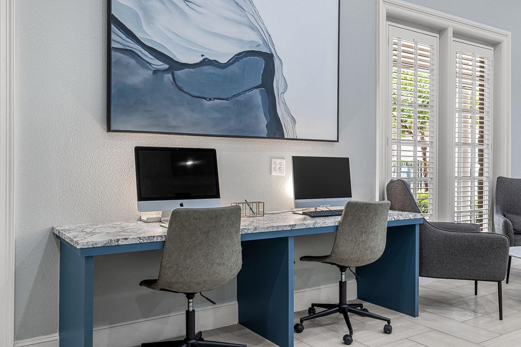 two desks with computers and chairs in a room with windows