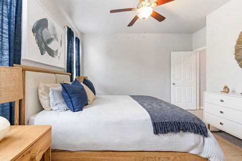 A bedroom with a bed, a ceiling fan, and a nightstand.