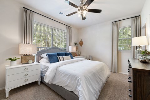A bedroom with a large bed, a ceiling fan, and a nightstand with a plant on it.