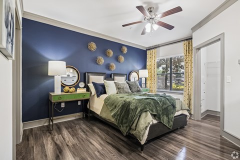 A bedroom with a bed, a table with a lamp, and a ceiling fan.