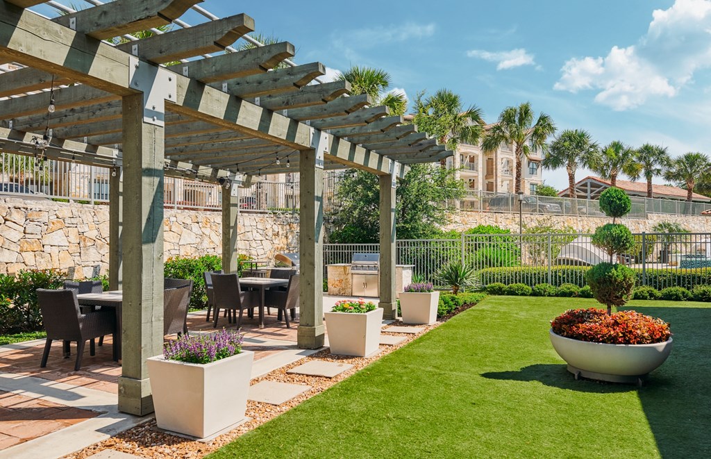 A patio with a table and chairs under a wooden pergola.