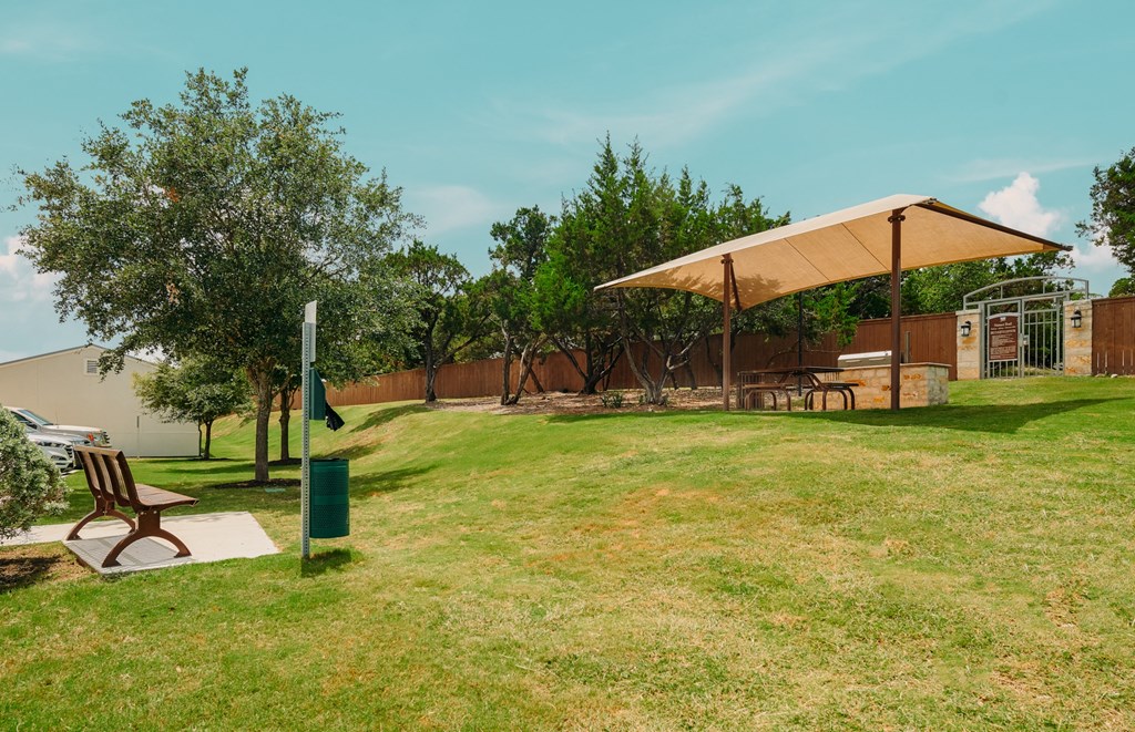 A park with a bench and a green trash can.