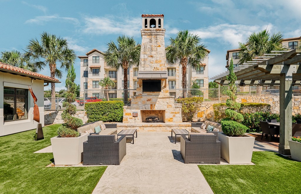 A patio with a fireplace and seating area in front of a building with a tower.