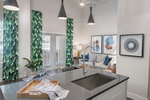 A modern kitchen with a sink, a window with curtains, and a dining table with glasses on it.