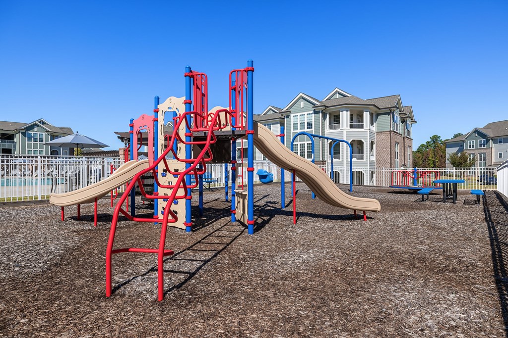 A playground with a red and blue slide in front of a house.