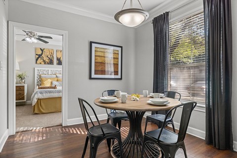 A dining room with a table set for two and a view of a bedroom through the window.