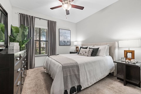 A bedroom with a large bed, a ceiling fan, and a window with curtains.