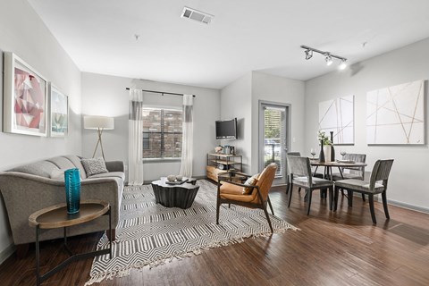 A living room with a grey couch, a coffee table, a dining table with chairs, and a television.