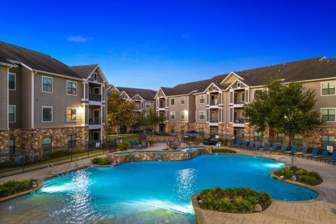 A swimming pool surrounded by a stone wall and chairs in front of apartment buildings.
