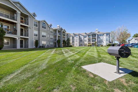A mailbox sits on a concrete slab in front of a grassy area with apartment buildings in the background.