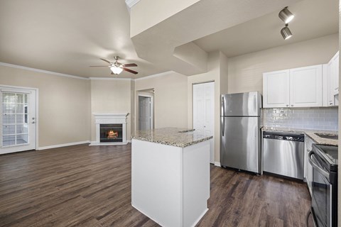 A kitchen with a stainless steel refrigerator and oven, and a fireplace in the living room.