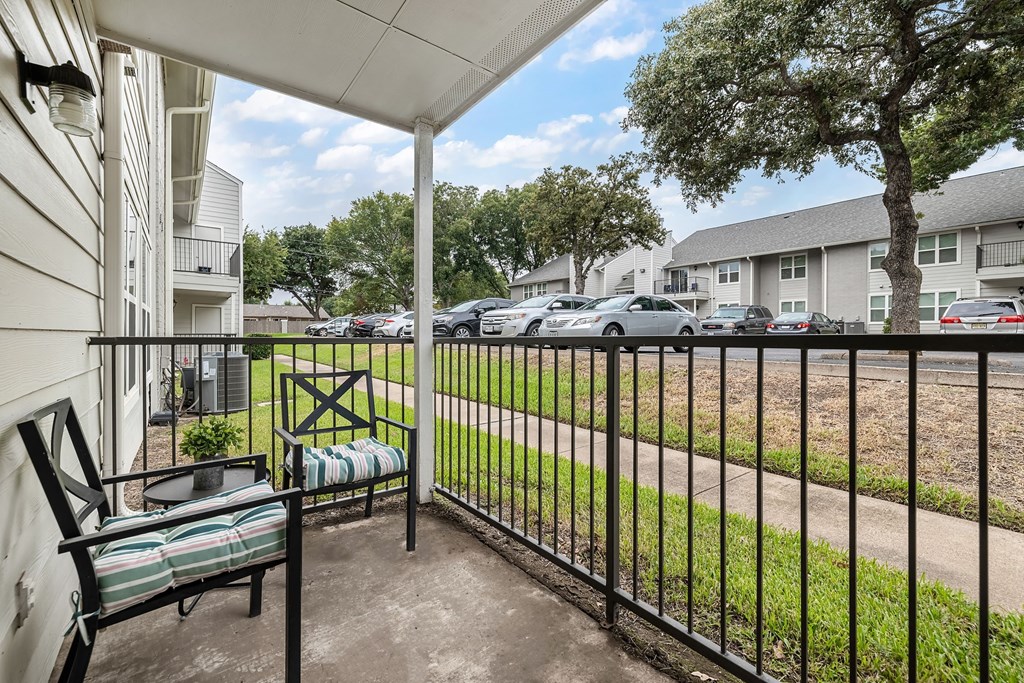 a patio with a chair and a fence overlooking a parking lot