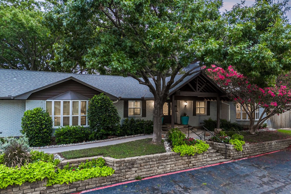 the front of a house with a stone retaining wall and trees
